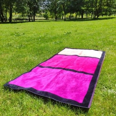 Toalha rosa, branca e preta estendida na relva num parque com árvores ao fundo