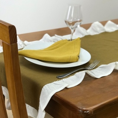 Mesa de madeira clara com toalha de mesa verde oliva e branca, prato branco com guardanapo amarelo e garfo e copo