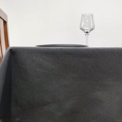 Mesa com toalha preta, prato cinzento e copo de vidro transparente