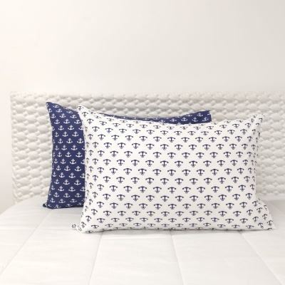 Duas almofadas com padrão de âncoras em branco e azul, sobre colchão branco com cabeceira acolchoada