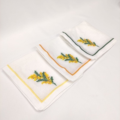Três toalhas brancas bordadas com flores amarelas e bordas coloridas