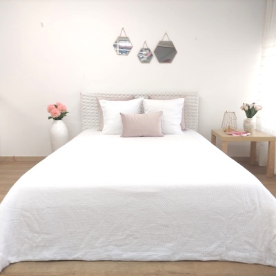 Cama de casal com roupa de cama branca, almofadas e espelhos hexagonais na parede.