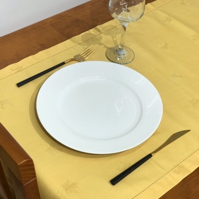 Conjunto de prato branco, talheres com cabos pretos, copo de vidro e toalha de mesa amarela sobre mesa de madeira