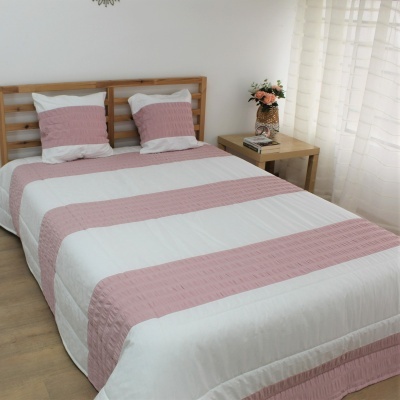 Colcha de cama dupla em riscas rosa e branco acolchoada com almofadas combinando e mesa de cabeceira com flores.