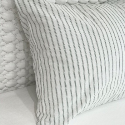 Almofada branca com riscas finas cinzentas em cima de colchão branco com manta de pontos grossos