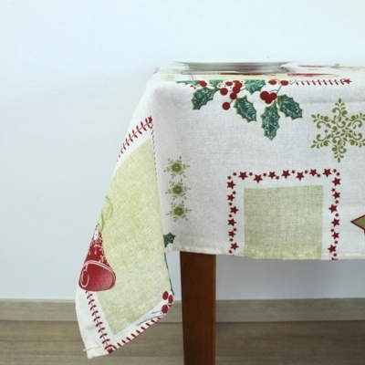 Toalha de mesa natalícia em algodão com estampados de azevinho e sinos colocada sobre mesa de madeira