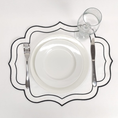 Jogo de jantar com prato branco, talheres inox e copo de vidro sobre suporte decorativo branco e preto