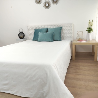 Cama com cobertura branca e almofadas verdes numa decoração minimalista branca com mesas de cabeceira e plantas