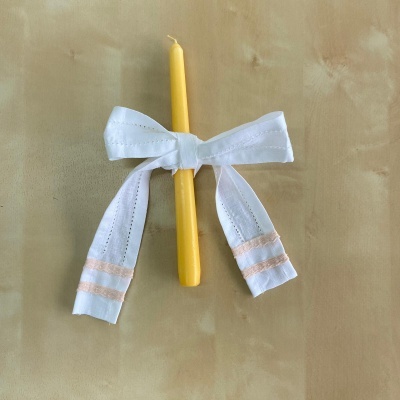 Vela amarela com fita branca e detalhes cor de rosa sobre superfície bege