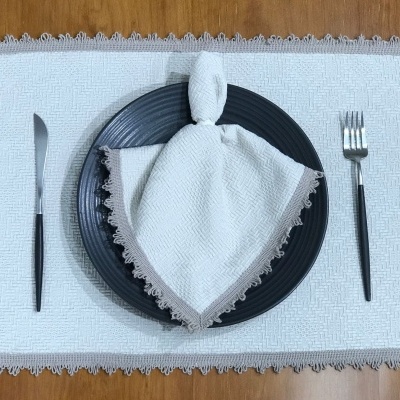 Conjunto de mesa com prato preto, guardanapo branco, talheres pretos e base branca com borda cinza sobre mesa de madeira