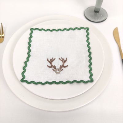 Guardanapo branco com borda verde e bordado de crânio com chifres sobre prato branco
