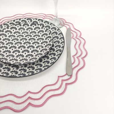 Conjunto de pratos com padrão preto e branco, guardanapo com borda rosa e talher metálico sobre mesa branca