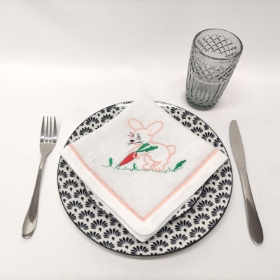 Mesa posta com prato decorado, guardanapo bordado com coelho, talheres e copo de vidro