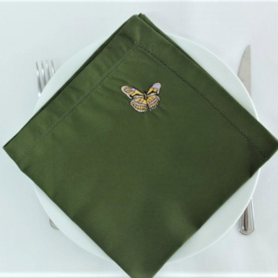 Guardanapo verde com bordado de borboleta sobre prato branco com talheres