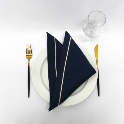 Prato branco com guardanapo azul e talheres dourados em fundo branco