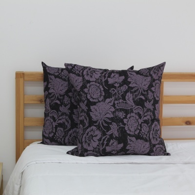 Almofadas decorativas florais lilás e preto em cama com cabeceira de madeira