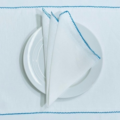Guardanapo branco com borda azul e prato branco sobre individual branco com borda azul