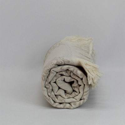 Manta bege enrolada com franjas sobre fundo cinzento