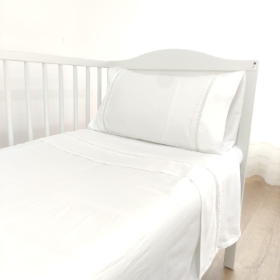 Cama de bebé branca com roupa de cama branca e rendados