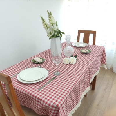 Mesa com toalha xadrez vermelha e branca, pratos, copos, talheres, jarra e vaso com flores