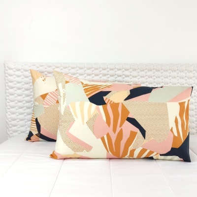Duas almofadas retangulares com padrão geométrico colorido em cama branca