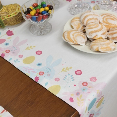 Toalha de mesa branca com padrão colorido de flores e orelhas de coelho e mesa com bolachas e doces