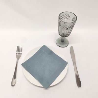 Conjunto de talheres, prato branco com guardanapo azul claro e copo de vidro cinza padrão geométrico