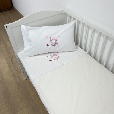 Cama de criança branca com lençol e fronha brancos bordados com personagem infantil rosa
