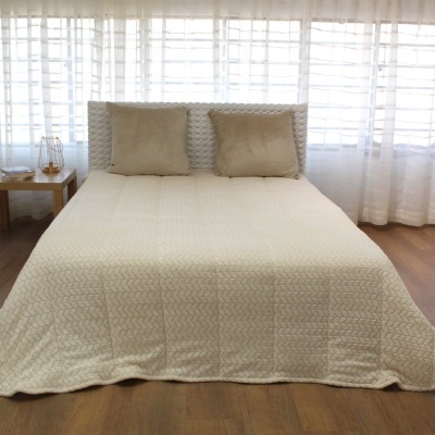 Cama com colcha creme e duas almofadas castanhas, em quarto com cortinas brancas e mesa de madeira