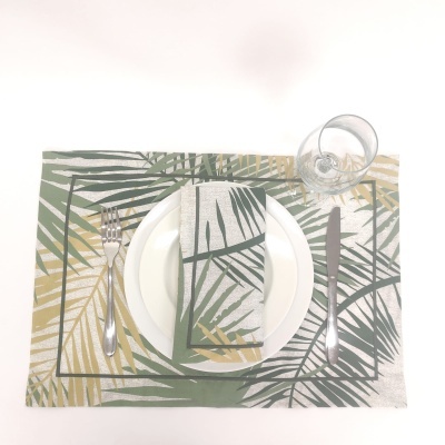 Jogo americano e guardanapo com padrão de folhas verdes e amarelas, prato branco, talheres e copo