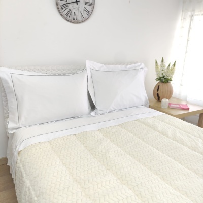 Cama com almofadas brancas, edredão creme texturado, relógio de parede e vaso com flores