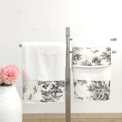 Toalhas brancas com bordado preto e creme em suporte metálico ao lado de vaso com flor cor-de-rosa