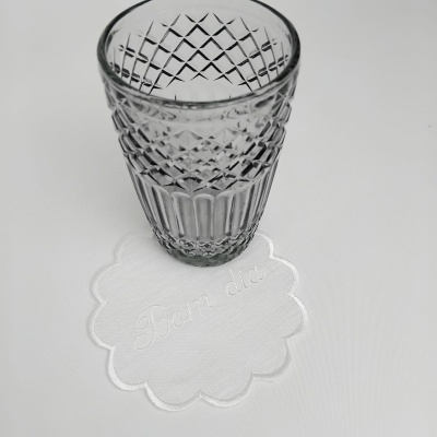 Copo de vidro transparente com padrão cruzado sobre guardanapo branco com texto 'Bom dia'