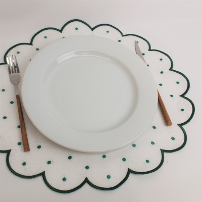 Prato branco redondo sobre individual branco com pontos verdes e talheres com cabo de madeira