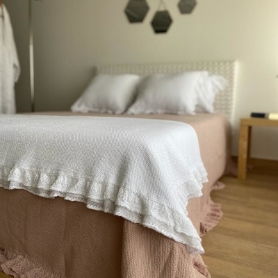 Cama com saia e colcha rosa claro com texturas e manta branca com folho numa decoração de quarto clara e moderna