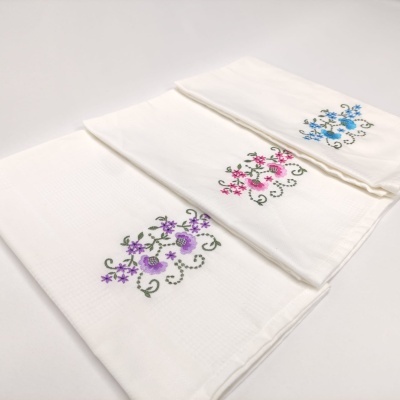 Três panos de cozinha brancos com bordados florais coloridos em padrão espiral