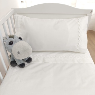 Cama de bebé branca com roupa de cama bordada e peluche cinza