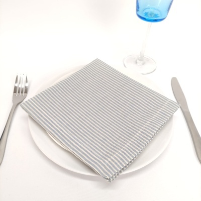 Guardanapo listrado cinza e branco sobre prato branco com talheres e taça azul