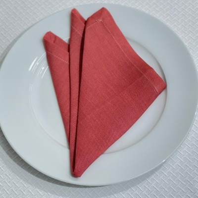 Guardanapo vermelho dobrado sobre prato branco em toalha texturizada.