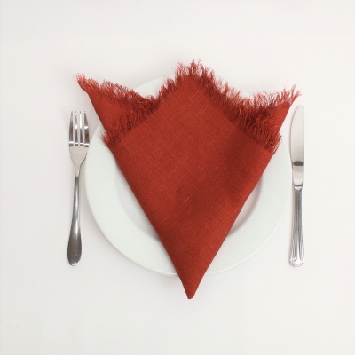 Guardanapo vermelho com franjas em prato branco, garfo e faca ao lado