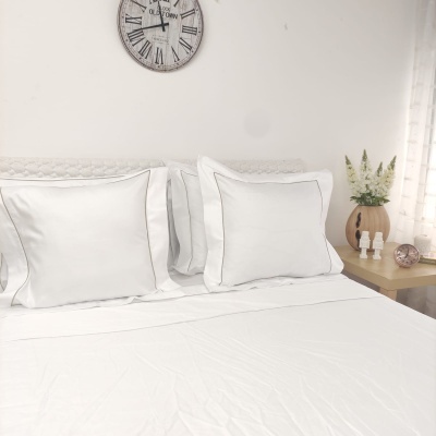 Cama com lençol e fronhas brancas, relógio de parede e mesa de cabeceira com vaso e objetos decorativos