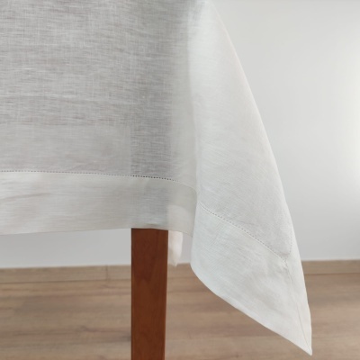 Toalha de mesa branca leve em tecido leve e semi-transparente pendurada numa mesa de madeira.