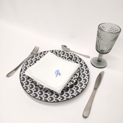 Conjunto de jantar com prato preto e branco, guardanapo bordado, talheres e copo cinza translúcido