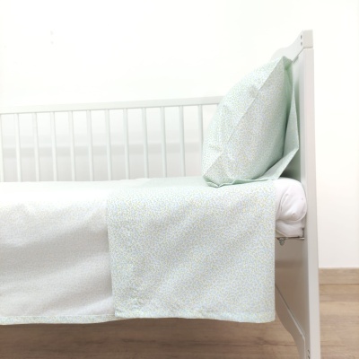 Cama de bebé branca com lençol e fronha com padrão esverdeado
