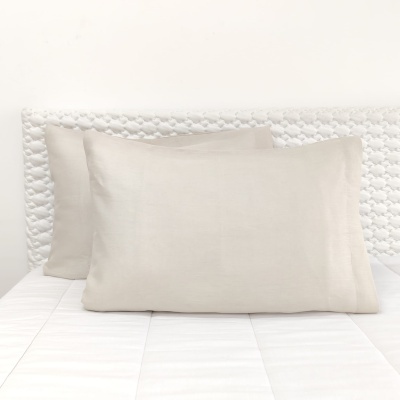 Almofadas retangulares bege claro sobre cama branca com cabeceira trançada