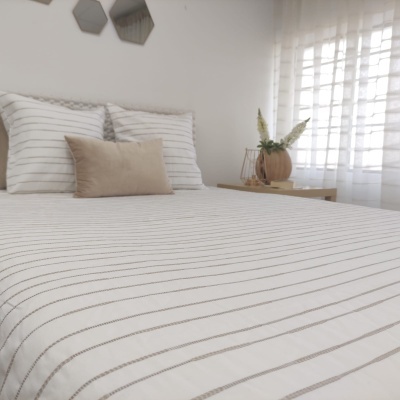 Edredão branco e cinza riscado com almofadas combinando em quarto iluminado