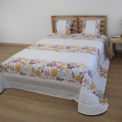 Colcha branca com estampado floral colorido num quarto com cabeceira e chão em madeira clara.