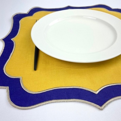 Jogo americano amarelo com borda azul e beige, prato branco e talher preto