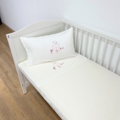 Berço branco com roupa de cama branca bordada com desenhos em rosa e vermelho