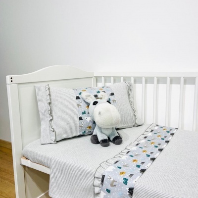 Berço branco com roupa de cama cinza e peluche cinzento